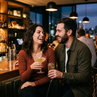 A couple enjoying cocktails at a bar in New Zealand, relaxed and flirtatious in a modern setting with warm lighting